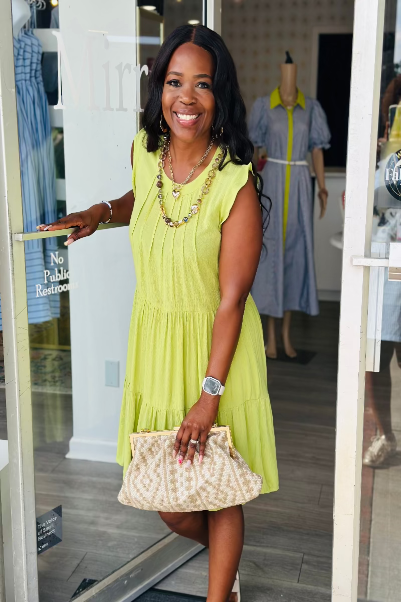Woman in a yellow dress standing in a store doorway, holding a clutch Mirror On Main Boutique