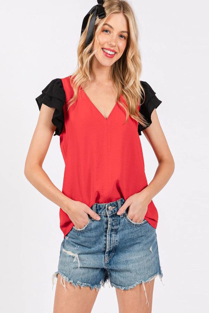 Woman wearing a red top with black sleeves and denim shorts on a white background
