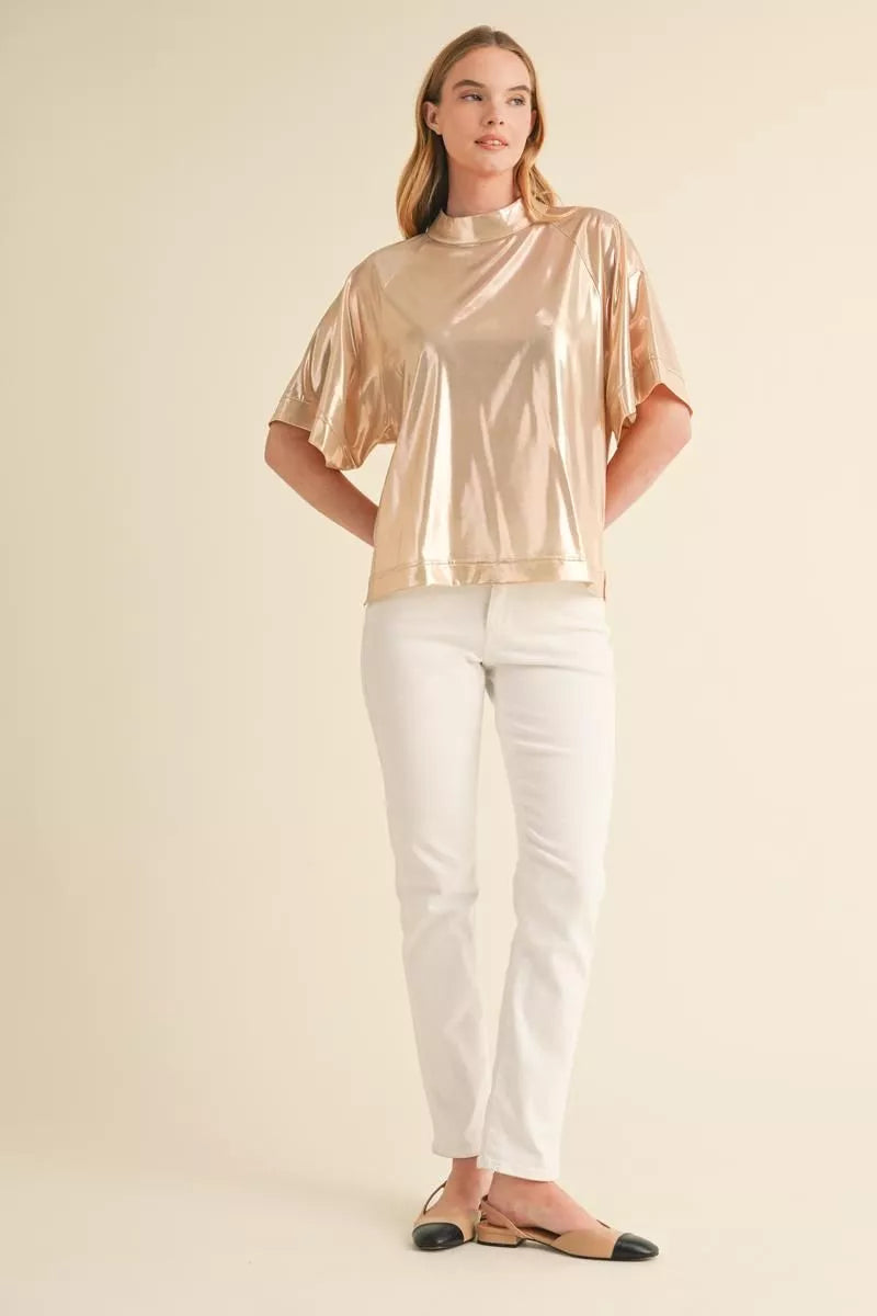 Model wearing rose gold metallic mock neck top with white pants – front view – Mirror On Main.