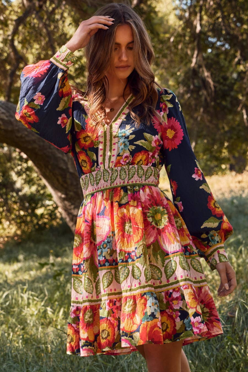 Woman wearing a colorful floral dress standing in a natural setting with trees and grass.