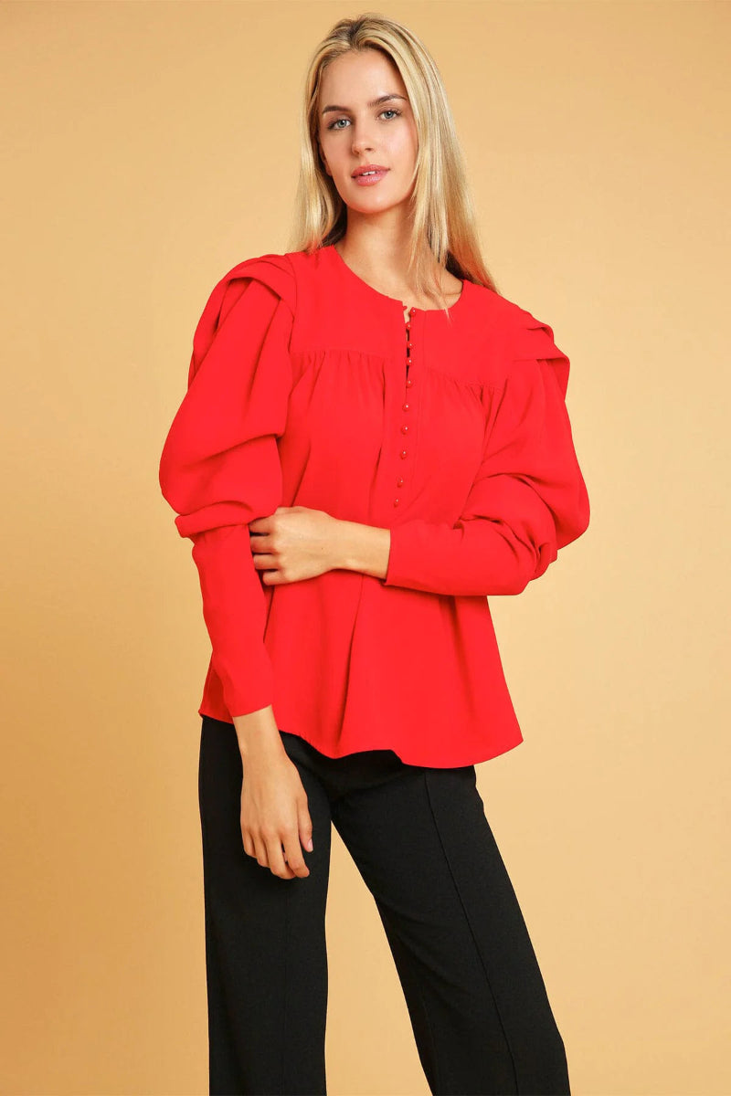 Woman wearing a red blouse with puffed sleeves against a beige background