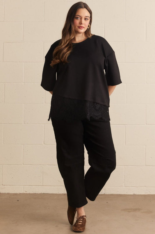 Plus size woman wearing a black short sleeve knit top with scallop lace hem detail, styled with black wide-leg pants — Mirror on Main