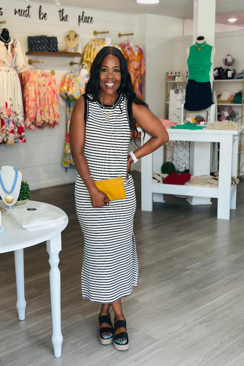 Woman in a striped dress standing in a store with clothing and accessories on display Mirror On Main Boutiue