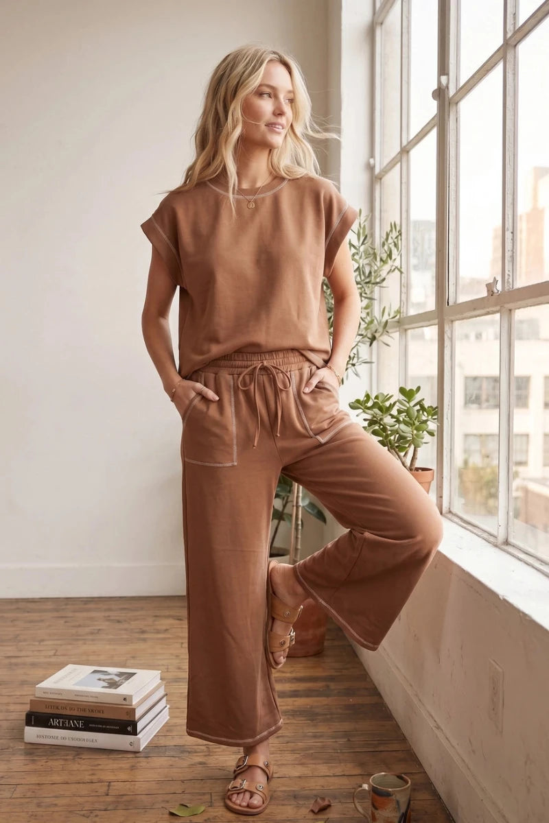 Woman in a brown outfit standing by a window in a bright room.