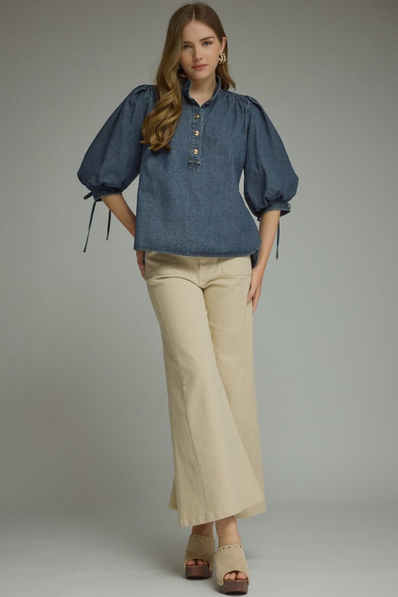Woman wearing a denim puff sleeve top with self-tie bow cuffs and ruffled stand collar, styled with cream wide-leg pants and block-heel clogs — Mirror on Main