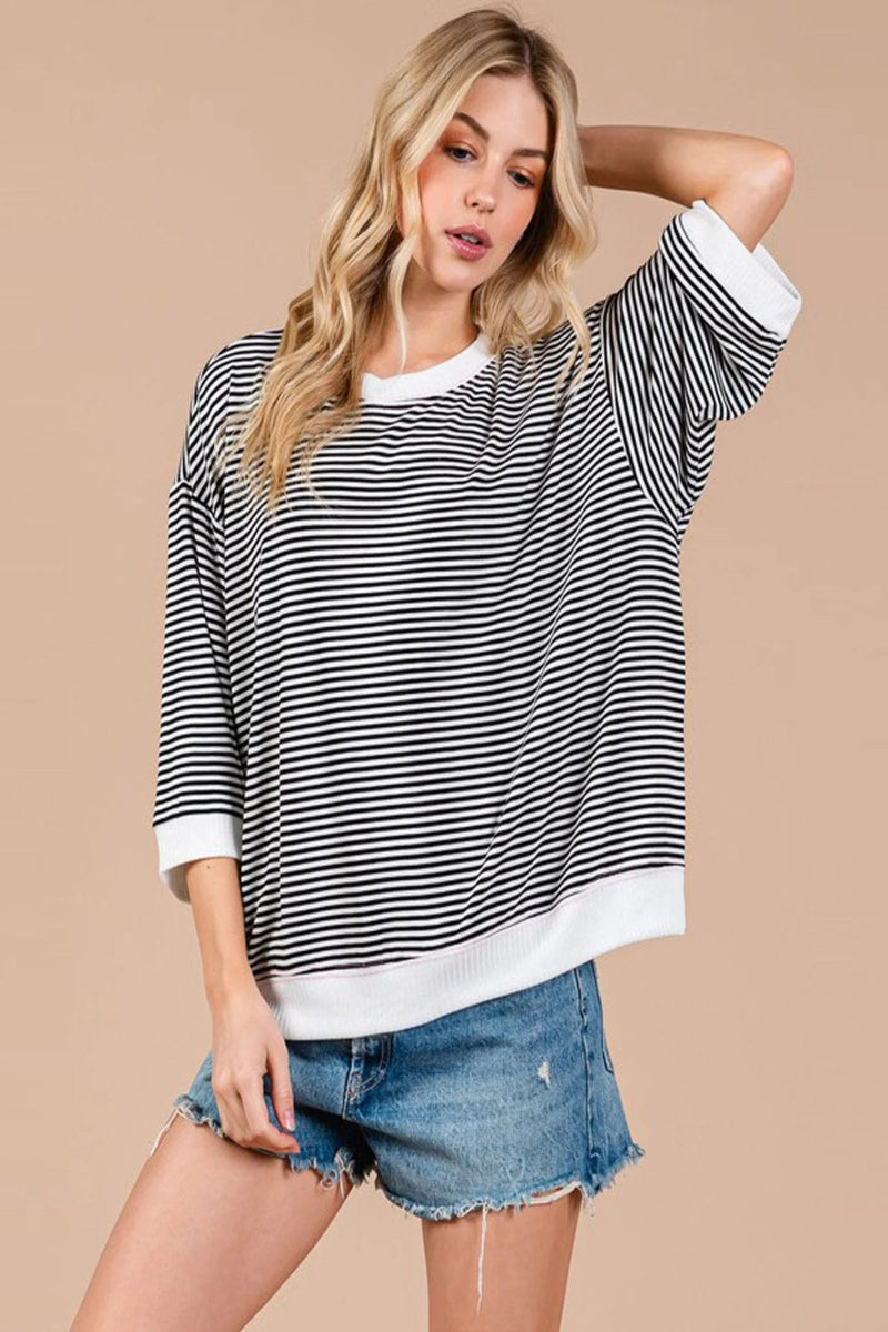 Woman wearing a black and white striped sweater with denim shorts on a beige background