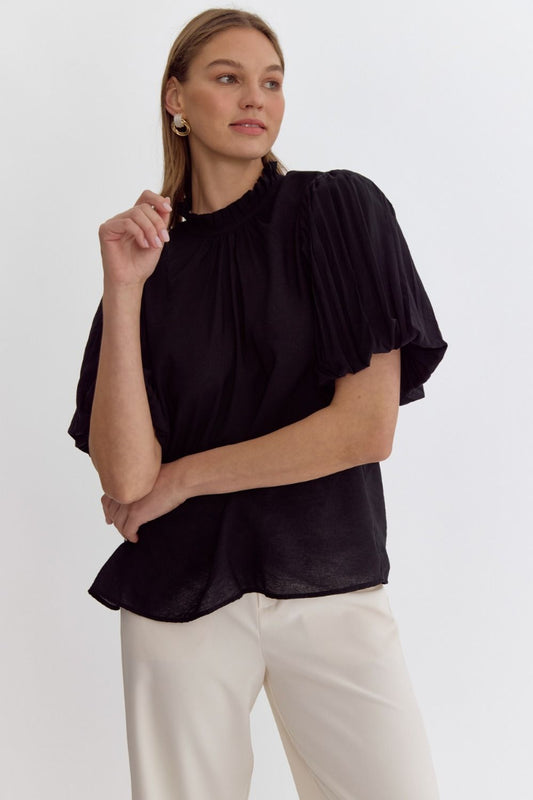 black cotton blouse with ruffle neckline and flutter sleeves styled with cream pants