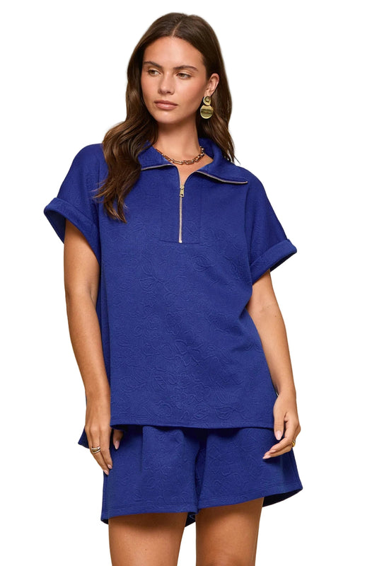 Blue textured two-piece set with dolman sleeve zip top and pleated shorts styled as a matching outfit.