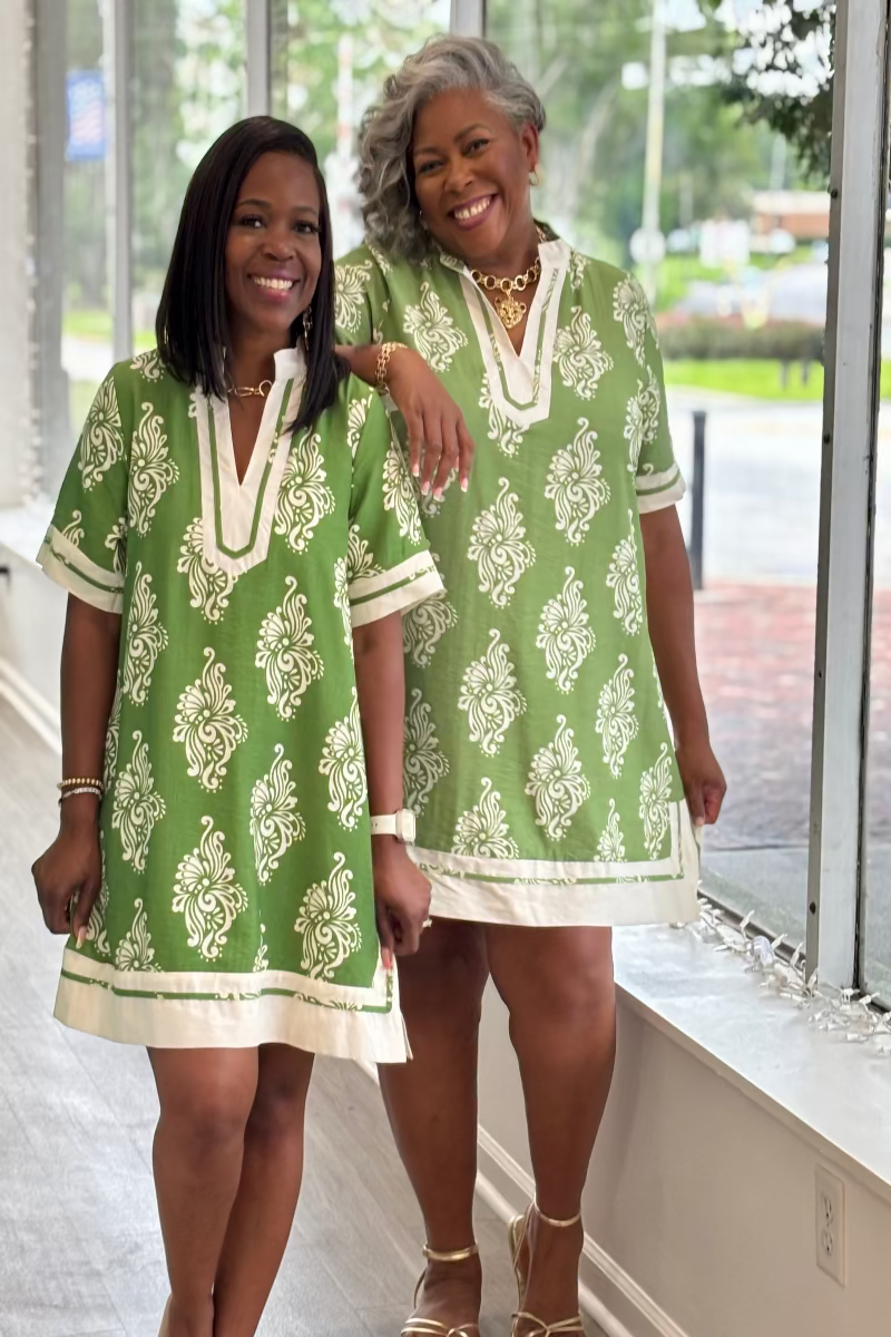Two women wearing green and white patterned dresses standing indoors Mirror On Main.