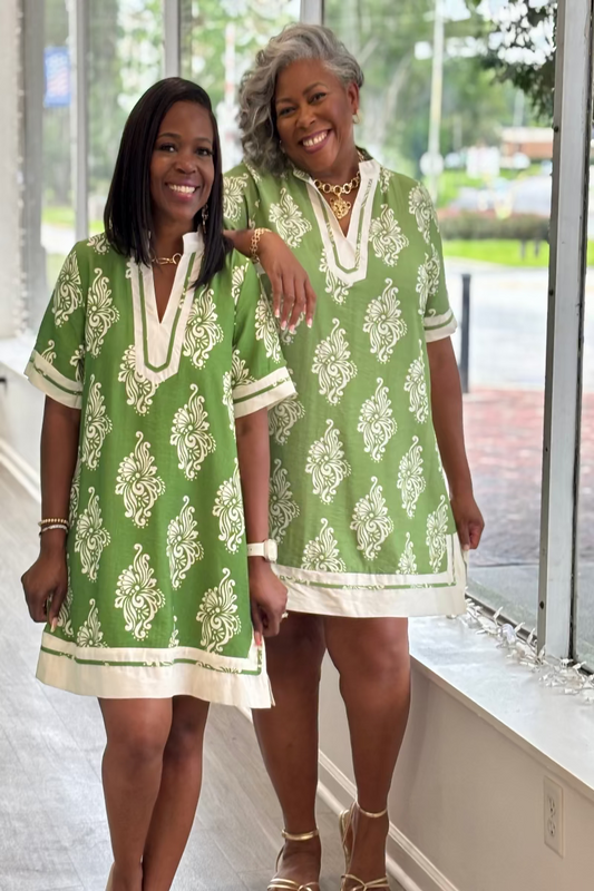 Two women wearing green and white patterned dresses standing indoors Mirror On Main.
