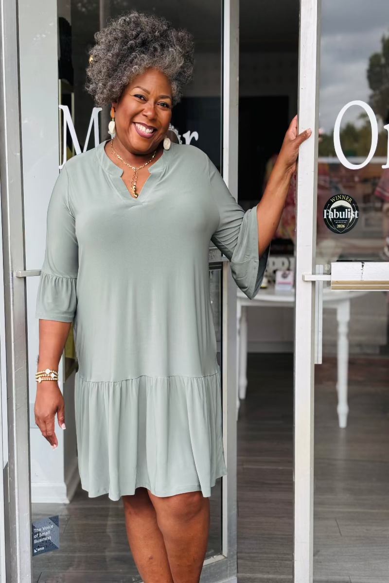Woman in a light green dress standing outside a store with glassdoors Mirror On Main.