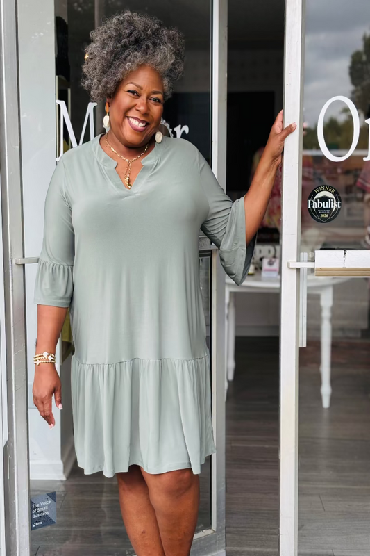 Woman in a light green dress standing outside a store with glassdoors Mirror On Main.