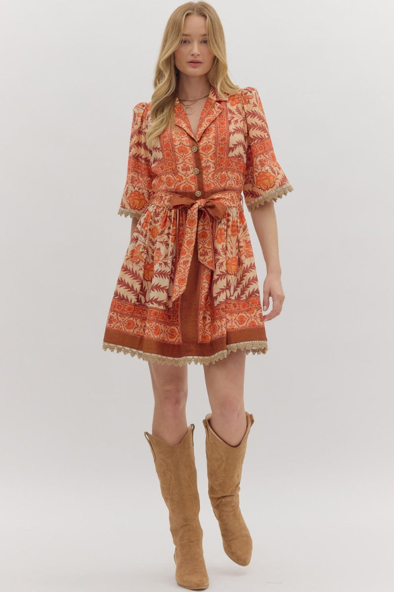 Woman wearing a patterned dress with a belt and tan knee-high boots on a white background