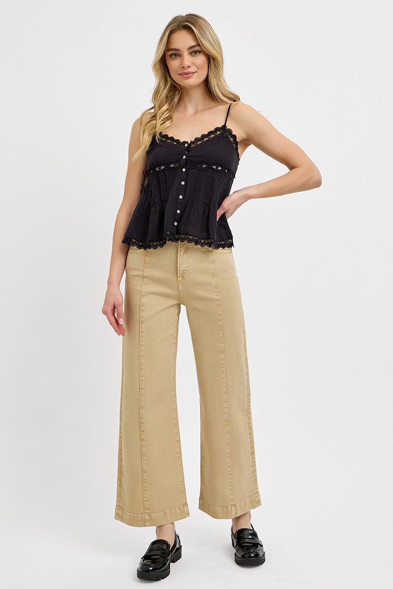 A woman modeling a black lace-trimmed camisole top and beige wide-leg cropped pants against a plain light gray studio background.