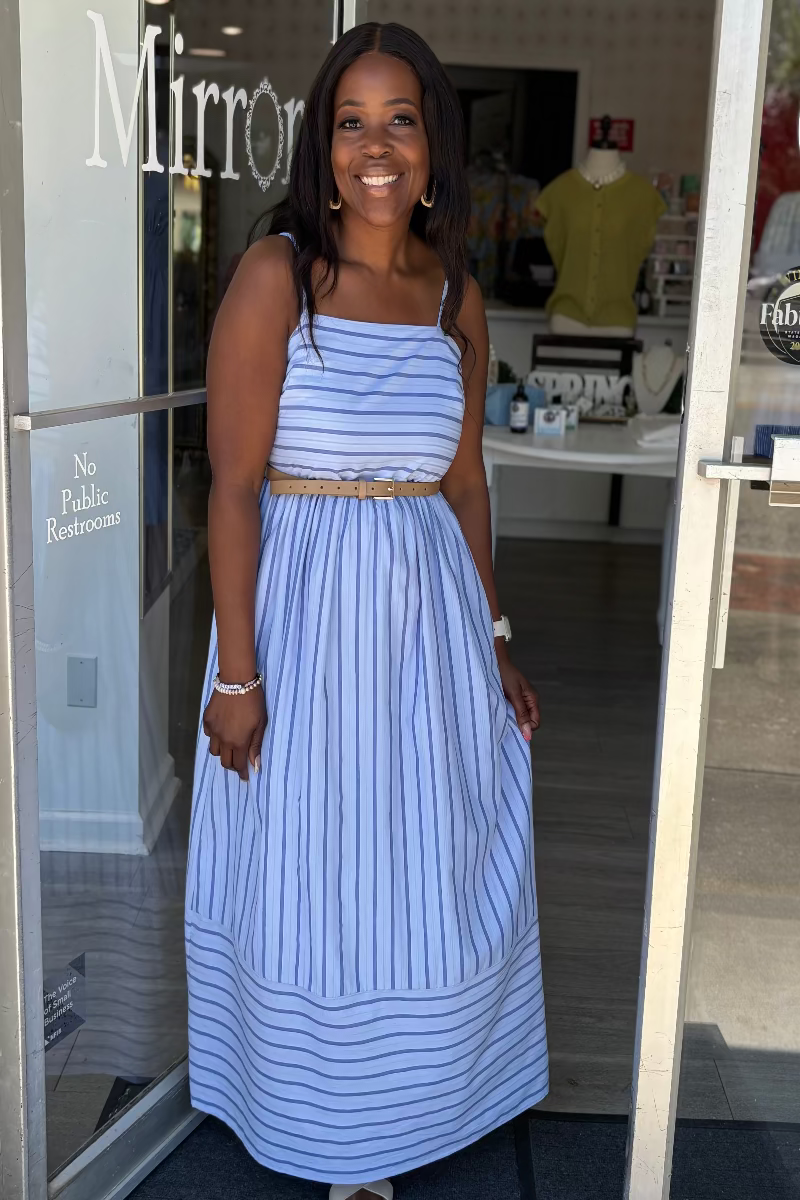 Woman in a blue striped dress standing outside a store with 'Mirror' displayed on the glass door.