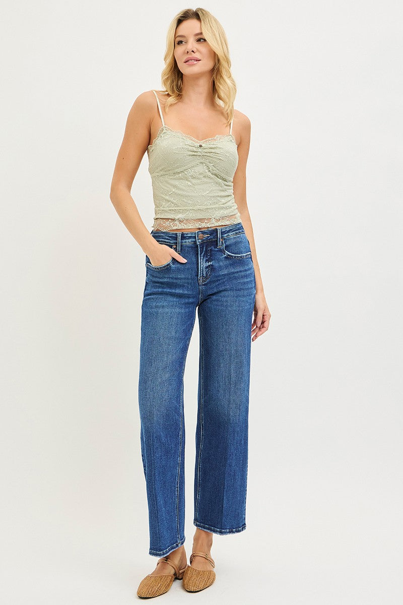 Woman wearing medium wash high rise tummy control ankle straight jeans with front crease line detail and raw frayed hem, styled with a sage lace cami and woven slide mules — Mirror on Main