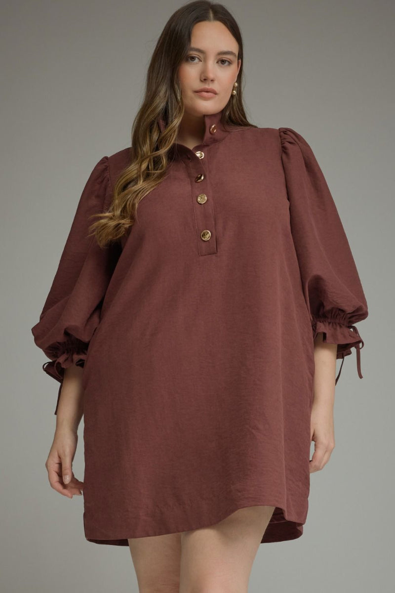 Plus size woman wearing a merlot balloon sleeve mini dress with stand collar, gold button closure, and adjustable ruffle tie cuffs — Mirror on Main