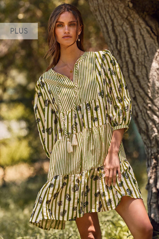 Woman wearing a green and white patterned dress standing outdoors near a tree.
