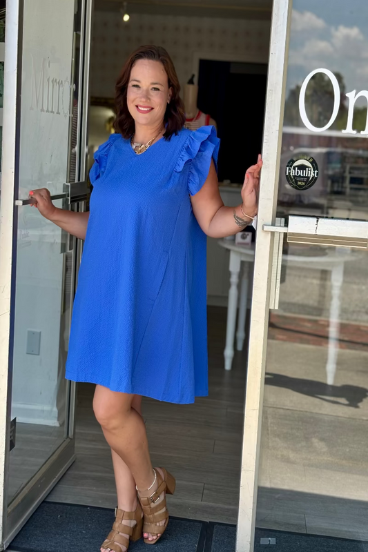 Woman wearing an ocean blue seersucker shift dress with ruffle sleeves and V-neckline — Mirror on Main