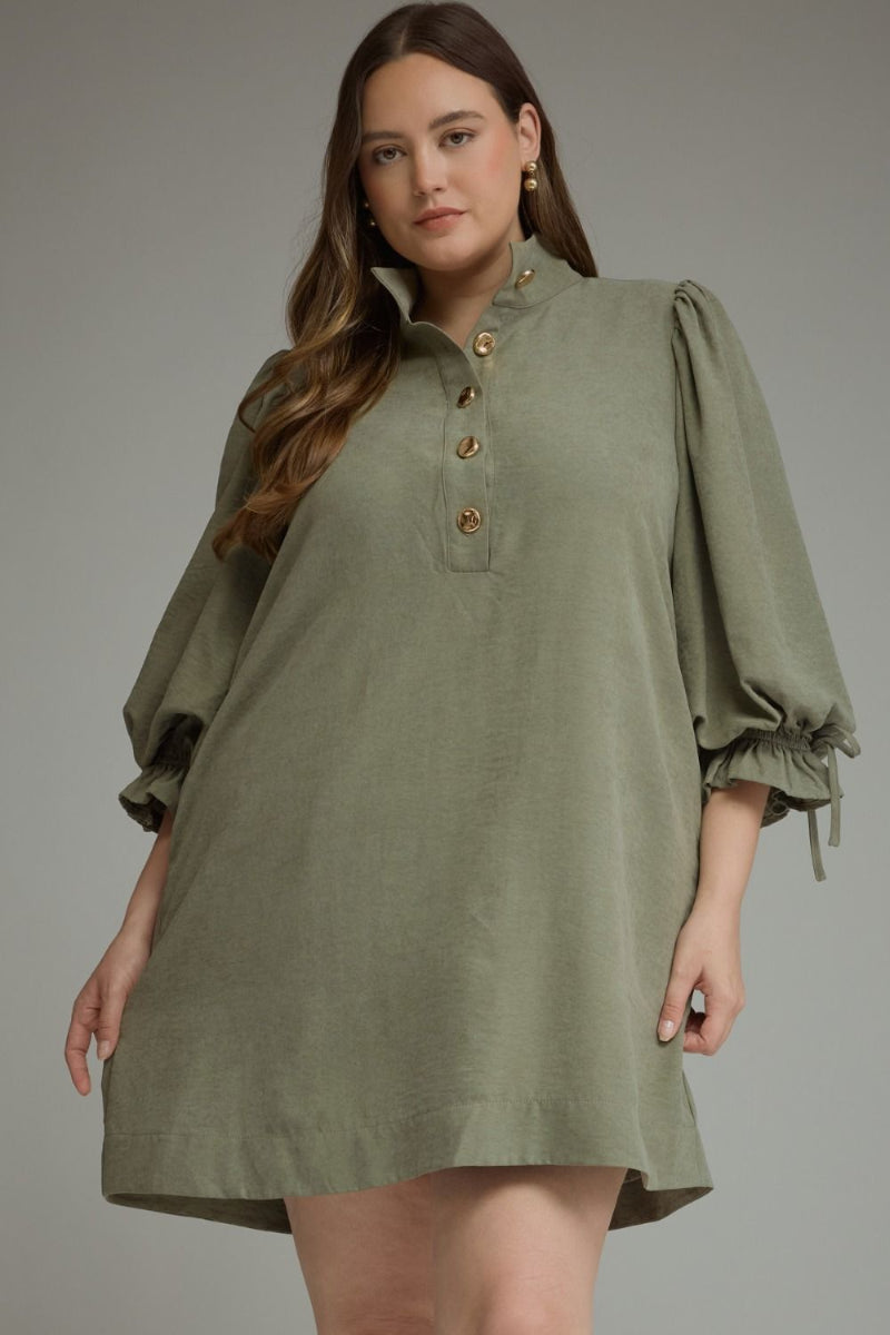Plus size woman wearing a sage olive balloon sleeve mini dress with stand collar, gold button closure, and adjustable ruffle tie cuffs — Mirror on Main