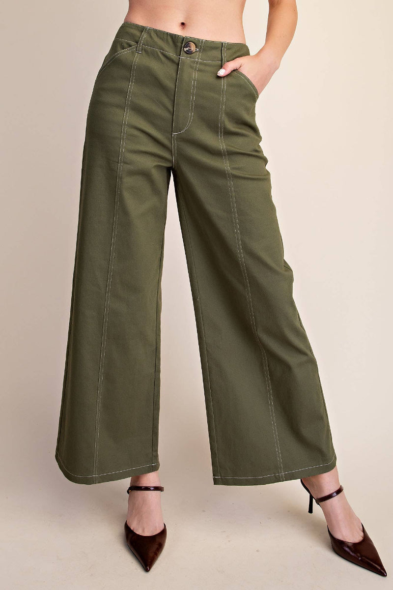 Woman wearing olive green high rise wide leg pants with contrast stitch seam detail and button fly closure, styled with brown heels — Mirror on Main