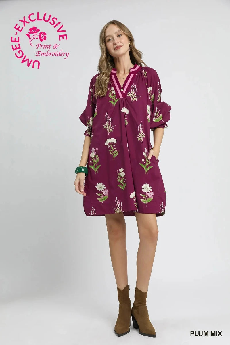 Woman wearing a plum floral tunic dress with contrast V-neckline trim and ruffle sleeve cuffs — Mirror on Main