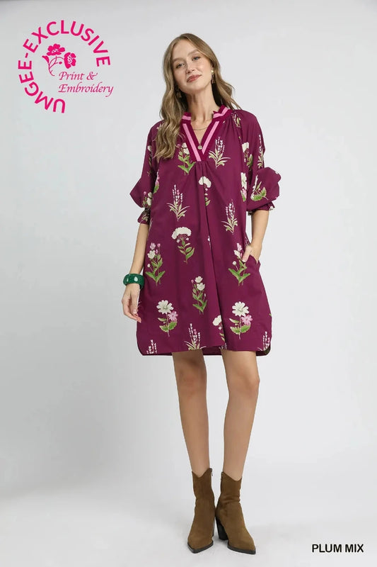 Woman wearing a plum floral tunic dress with contrast V-neckline trim and ruffle sleeve cuffs — Mirror on Main