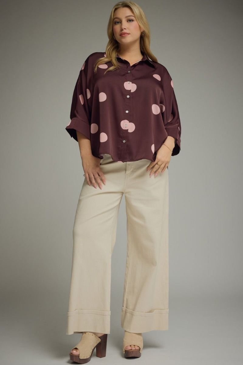 Plus size woman wearing a plum and blush pink polka dot collared button-front top with 3/4 sleeves, styled with cream wide-leg trousers and block-heel clogs — Mirror on Main