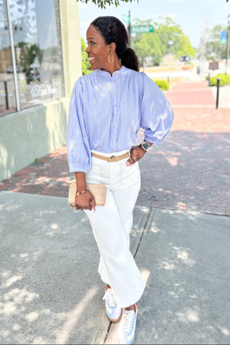Woman wearing a blue striped shirt and white pants standing outdoors on sidewalk