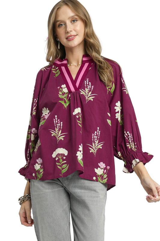 Woman wearing a plum-colored blouse with floral embroidery on a white background