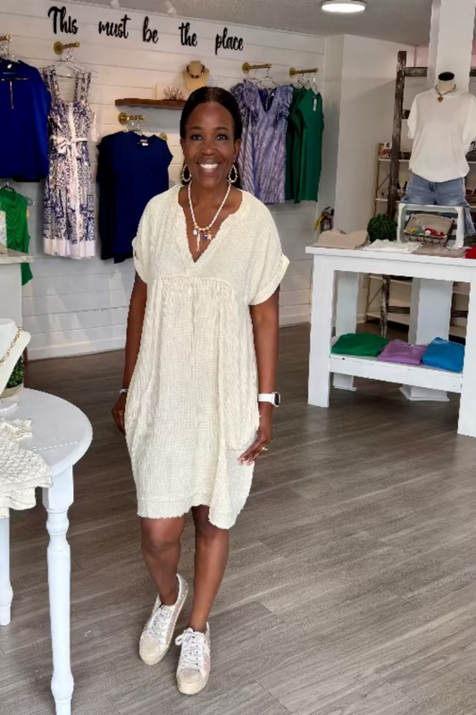 A woman modeling an off-white, long-sleeved, v-neck dress with a round neckline.