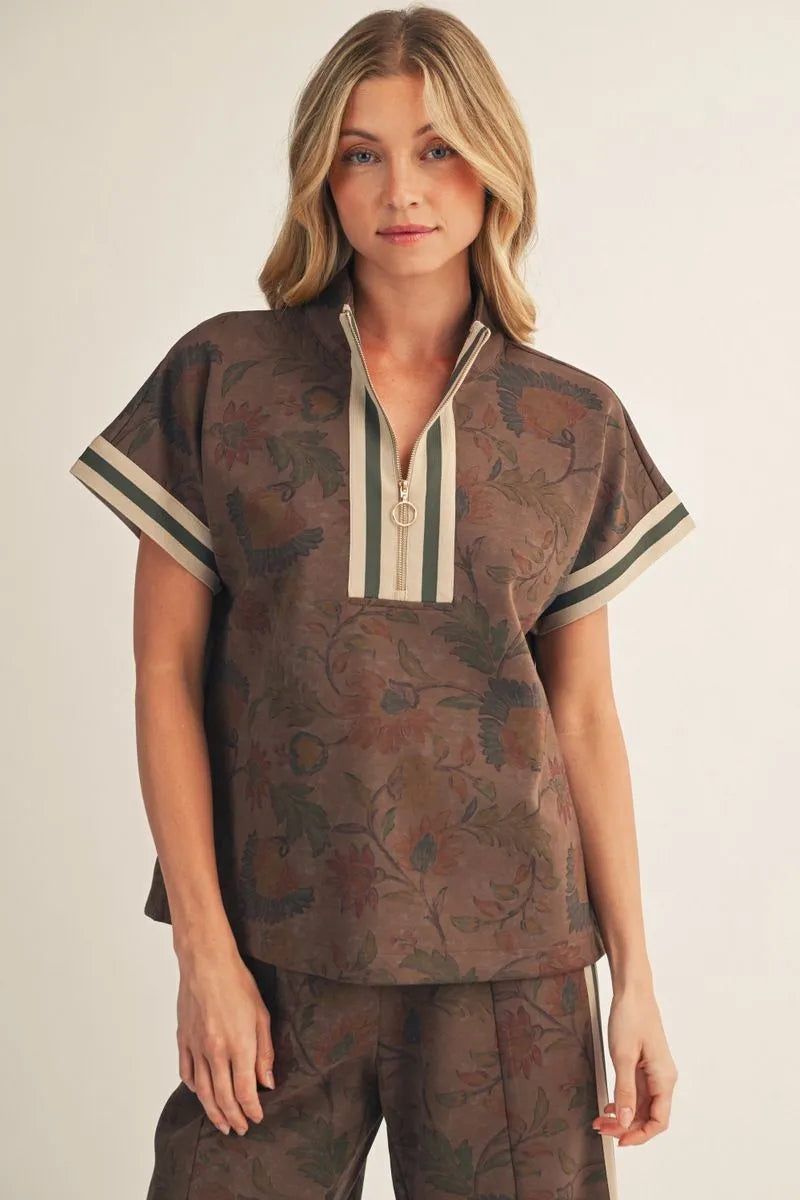 Women's brown floral print short-sleeve top featuring a zip-front neckline, drop shoulders, cream and olive contrast ribbed trim, and relaxed fit.