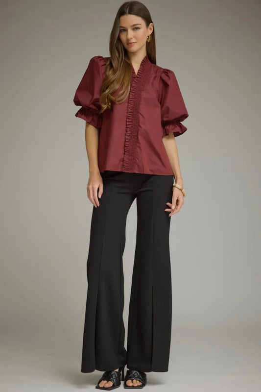 Plus size woman wearing a wine smocked ruffle V-neck puff sleeve top with elasticated ruffle cuffs, styled with black wide-leg flare pants — Mirror on Main