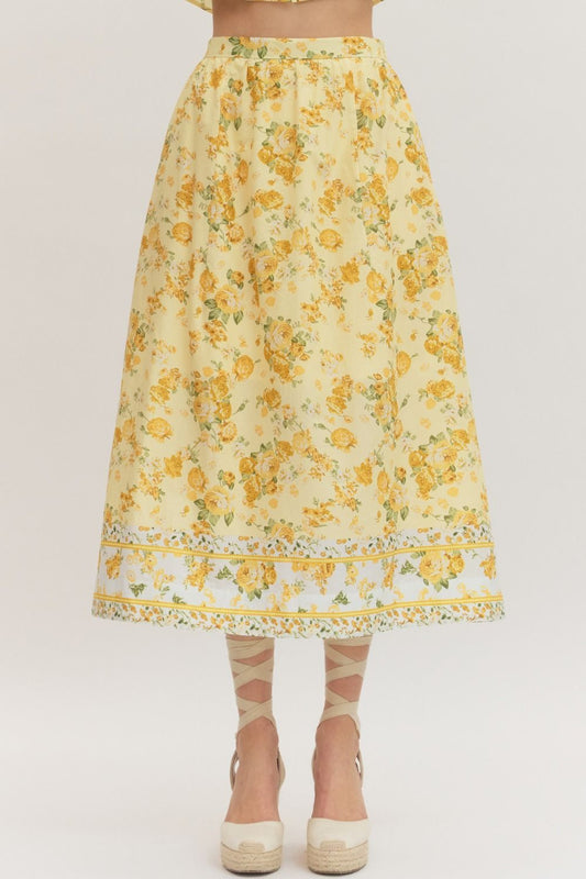Yellow floral cotton midi skirt with golden rose print, border print hem detail, A-line silhouette, and side zipper closure — styled with cream espadrille wedges