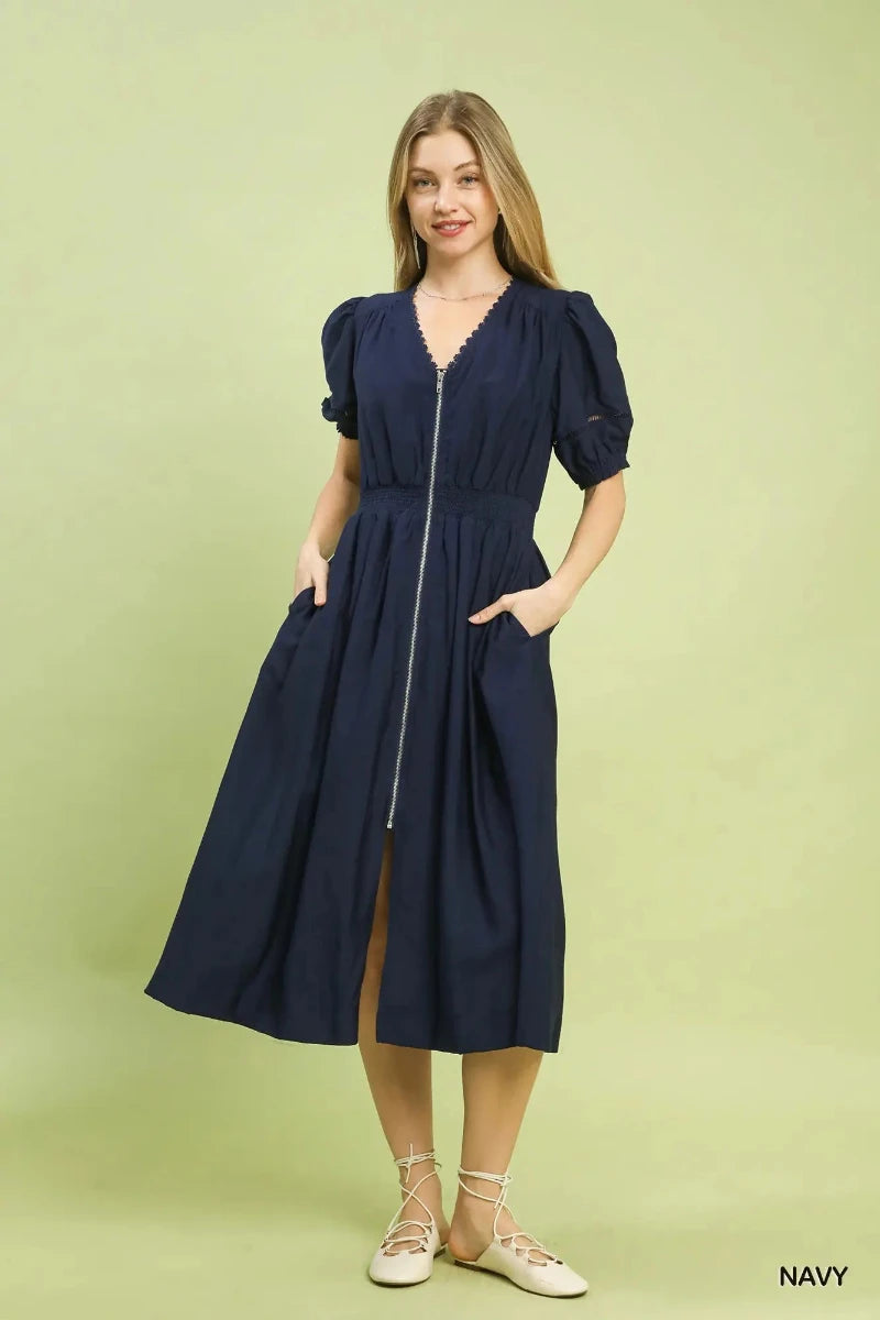 Woman wearing a navy zip front smocked waist midi dress with lace V-neckline and short puff sleeves, styled with white lace-up flats — Mirror on Main